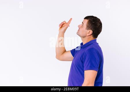 Sign language. Caaucasian man wearing casual clothes looks up and points up with index finger against white background with side ad space. Stock Photo