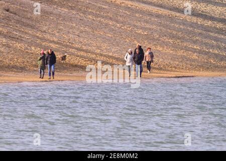 Haltern, NRW, Germany. 31st Jan, 2021. A few walkers stroll on the natural sand beach of 'Silbersee II' a popular swimming lake near Haltern on a beautifully sunny Sunday afternoon in the Muensterland. Germany has been in lockdown since November. Whilst most shops and services are closed, outdoor exercise and walking are allowed and encouraged, as long as social distancing is maintained. People from one household can exercise together or with one other person, distance of 1.5m needs to be maintained or a mask worn, otherwise penalties apply. Credit: Imageplotter/Alamy Live News Stock Photo