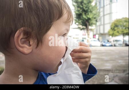 3 years boy blows his nose with tissue on the street. Closeup Stock Photo