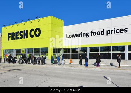 Ottawa, Canada - January 30, 2021: Customers stand in line, socially distanced, in the cold as they have to wait to for their turn to enter the Freshc Stock Photo