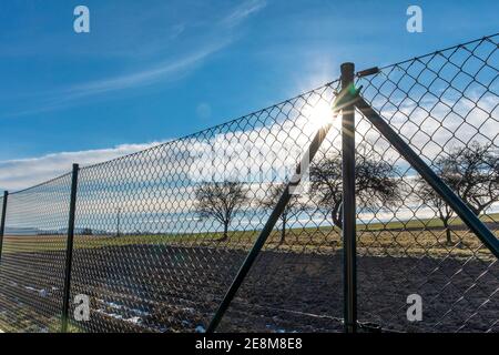 Wire metallic mesh fence around a football field. Blurred green grass ...
