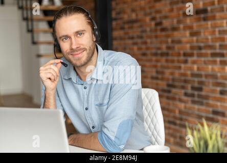 Millennial young male salesman in a headset is holding the microphone, hipster customer service representative posing against the brick wall, sitting Stock Photo