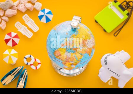 Miniatures of beach equipment, airplane and globe with world map on yellow background. Vacation travel concept Stock Photo