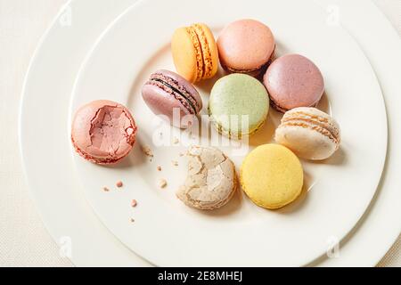 Multicolored delicious french macaroons or macarons lying in a light plate on a white table, top view Stock Photo