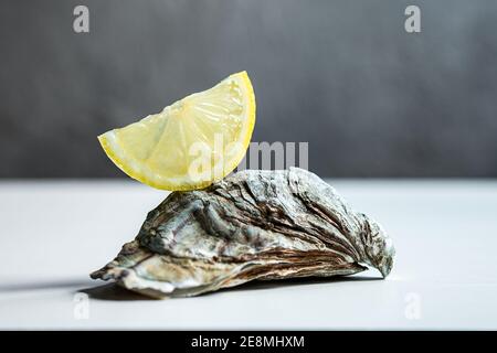 Closed fresh raw oyster on a white table with a slice of lemon close-up Stock Photo