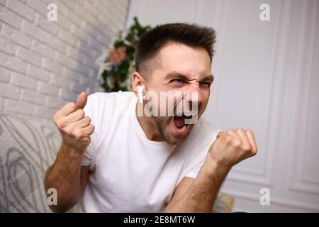 angry young man in earphones is talking to somebody on video call. man yelling Stock Photo