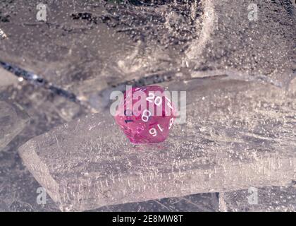Image of one pink 20 sided role playing die on a sheet of ice in the winter's sun Stock Photo