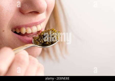 Young beauty woman eating a black caviar by spoon on the white background with copy space. Stock Photo