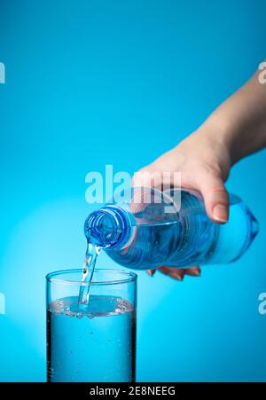 A transparent glass is filled with water from a plastic bottle on a light blue background. Stock Photo