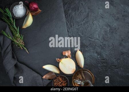 An empty, flat, rectangular dish, surrounded by onions, spices and rosemary on a black background. Stock Photo