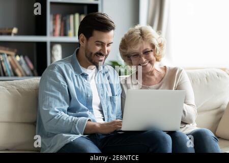 Happy young man teaching smiling older mother using computer apps. Stock Photo