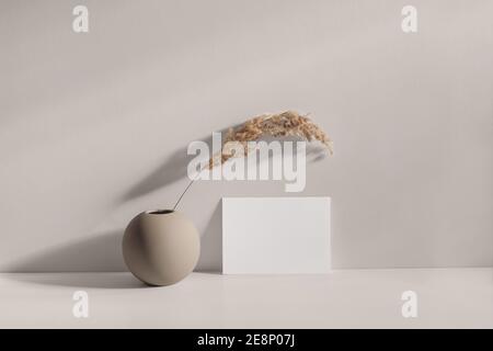 Modern summer stationery still life scene. Beige spheric vase with dry lagurus grass. Table background in sunlight. Blank paper card, invitation Stock Photo