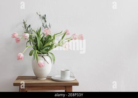 Romantic Easter, spring still life scene. Cup of coffee and floral bouquet in white ceramic vase on wooden bench. Feminine styled photo. Pink tulips Stock Photo