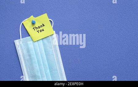 Thank you note on top of medical face mask. Pin on blue board. Copy space. Stock Photo