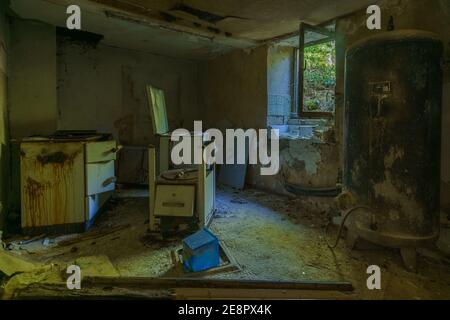 abandoned kitchen inside destroyed house with old rusty steel water tank Stock Photo