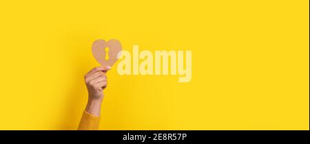 wooden heart with keyhole in hand over yellow background, panoramic image Stock Photo