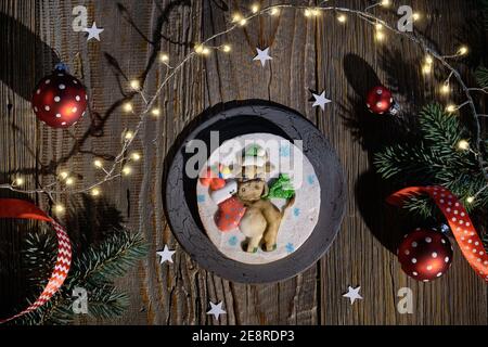 Ornate gingerbread decorated with silly funny cow with Xmas sock full of presents. Christmas flat lay with fir twigs, red baubles and festive lights Stock Photo