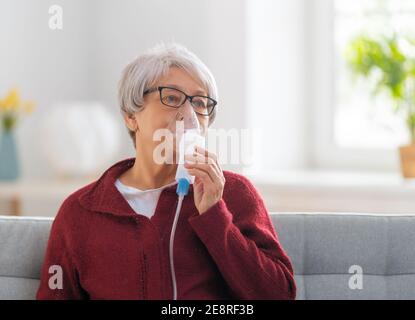 Elderly woman using inhaler for asthma and respiratory diseases at home. Stock Photo