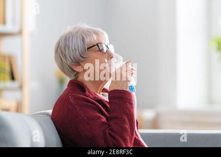 Elderly woman using inhaler for asthma and respiratory diseases at home. Stock Photo