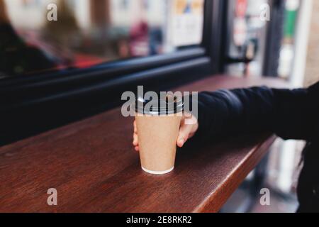 Girl holds a paper cup of coffee in hand near cafe Stock Photo