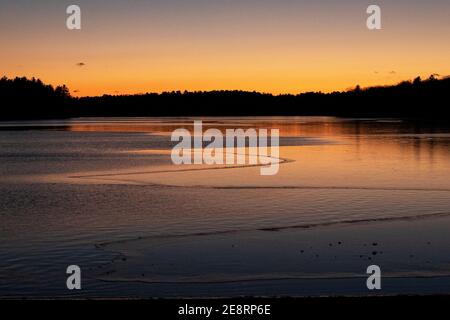 Winter sunset over partially frozen water at Long Lake in Littleton, Massachusetts, USA. Stock Photo