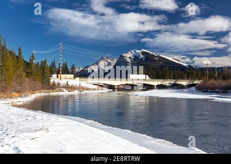 Trucks Passing over Alberta Bow River Bridge on Trans Canada Highway 1 or Highway One with Distant Snowy Peaks of Canadian Rocky Mountains on Horizon Stock Photo