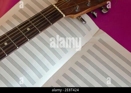 Acoustic guitar fingerboard head and an open notebook on a purple background. Musical creativity. Selective focus Stock Photo