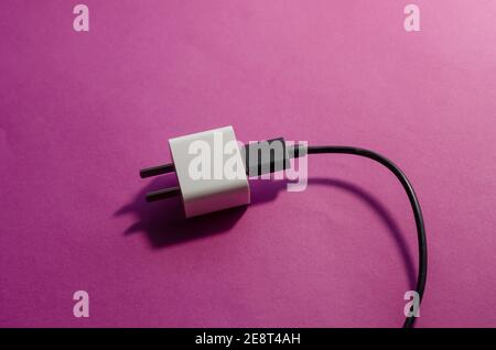 White Smartphone charger adapted for the USA with a black date cable on a pink background. DC wall adapter and USB data cable. Selective focus. Stock Photo