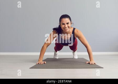Happy smiling woman looking at camera while doing push-ups on sports mat at the gym Stock Photo