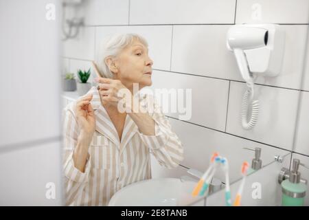 Gray-haired woman brushing her hair in the bathroom Stock Photo