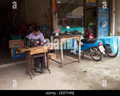 A tailor man is using his sewing machine in front of his worn-out stall Stock Photo