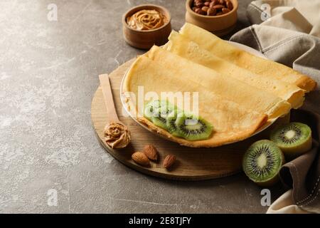 Concept of breakfast with crepes with kiwi, peanut butter and nuts on gray background Stock Photo