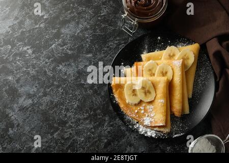 Concept of delicious breakfast with crepes with sugar powder and banana on black smokey background Stock Photo