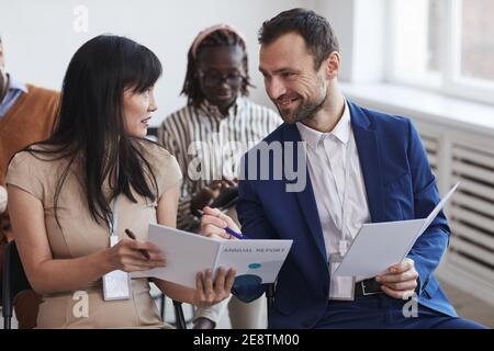 Multi-ethnic group of people in audience at business conference focus on smiling man and woman talking while sitting on chairs Stock Photo