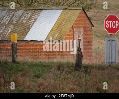 bright red Stop sign at a tank crossing and road junction with a disused red brick building across the road on Salisbury Plain, Wiltshire Stock Photo