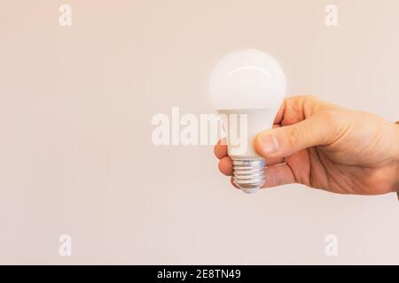 Man hand holding illuminated light bulb against beige background Stock Photo