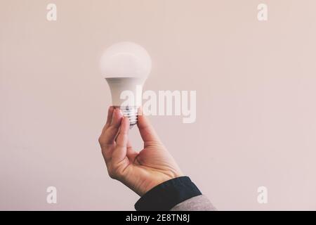 Female hand holding illuminated light bulb against beige background Stock Photo