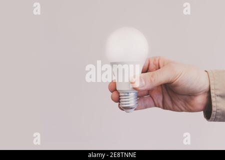 Man hand holding illuminated light bulb against beige background Stock Photo