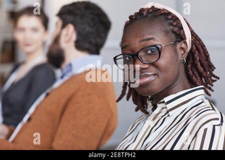 Close up portrait of young African-American woman wearing glasses and looking at camera while sitting in audience at business conference or seminar, c Stock Photo