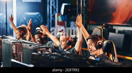 Celebrating success. Team of happy professional cyber sport gamers giving high five to each other while participating in eSports tournament. Video games online competition Stock Photo