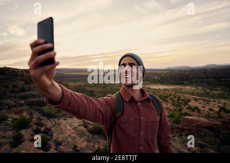 Portrait of happy young man taking selfie on smartphone against morning sunrise Stock Photo