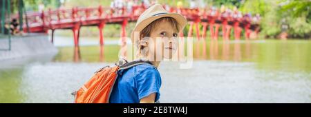 BANNER, LONG FORMAT Caucasian boy tourist on background of Red Bridge in public park garden with trees and reflection in the middle of Hoan Kiem Lake Stock Photo