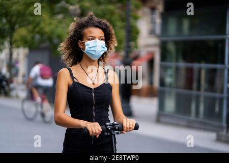 young woman wearing a mask riding her scooter in the city Stock Photo