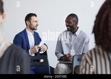 Portrait of two smiling businessmen talking while sitting on chairs in audience at business conference or seminar, copy space Stock Photo