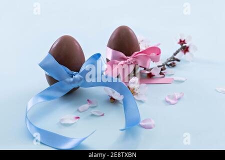 Appetizing chocolate eggs with different colored ribbons surrounded by cherry blossoms. Selective focus and close up. Easter holidays concept. Stock Photo