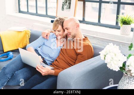 Shot of happy couple sitting on couch at home and using laptop while relaxing at home. Stock Photo