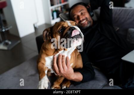 Middle aged man relaxing on the sofa and listening to music next to his dog Stock Photo