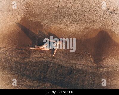 young woman with red hair in a bathing suit lies in the clear coastal water of the sea with a sandy bottom top view shooting drone Stock Photo