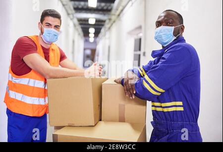 Two warehouse workers with face masks because of Covid-19 with packages in the warehouse Stock Photo
