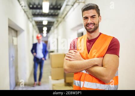 Smiling foreman or warehouse clerk with safety vest in the warehouse of a haulage company Stock Photo